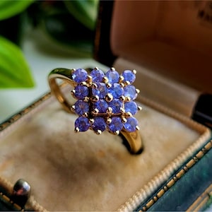 May include: A gold ring with a cluster of purple gemstones set in a square shape.