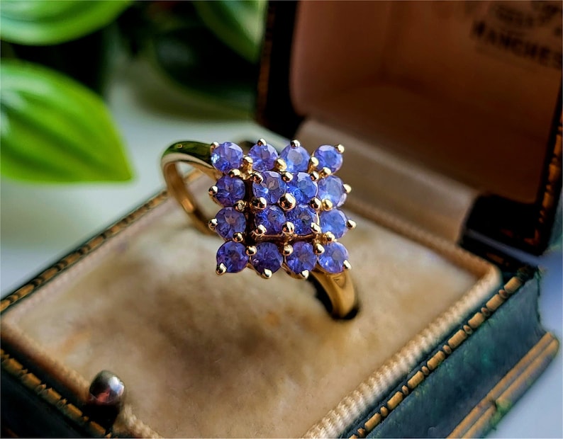 May include: A gold ring with a cluster of purple gemstones set in a square shape.