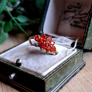 May include: A gold ring with a cluster of red gemstones set in a floral design. The ring is in a green velvet ring box.
