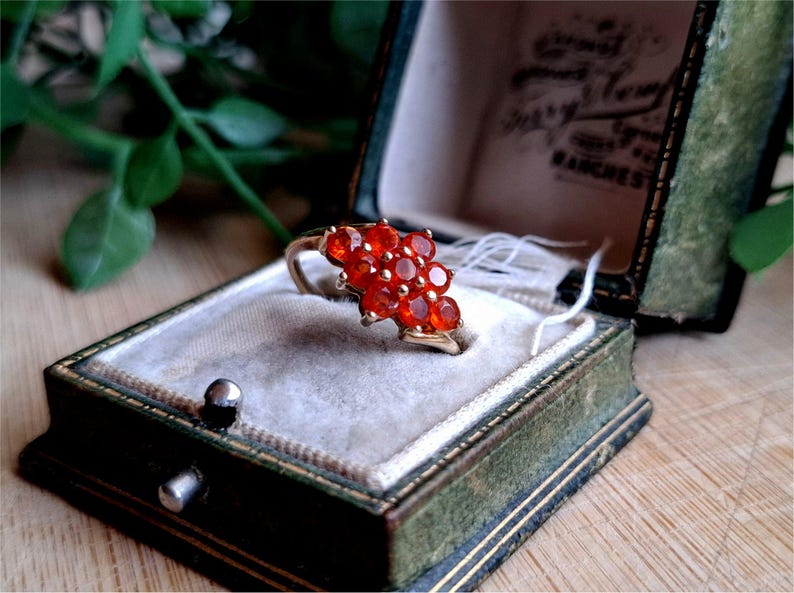 May include: A gold ring with a cluster of red gemstones set in a floral design. The ring is in a green velvet ring box.