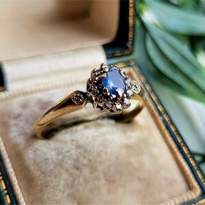 Pode incluir: Um anel de ouro com um safira azul cercado por uma halo de pequenos diamantes.