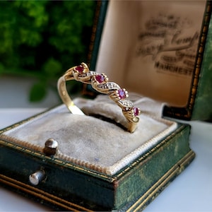 May include: A gold band ring with a twisted design set with five red rubies and small diamonds. The ring is in a green velvet ring box.