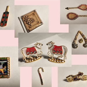 May include: A collection of miniature gold-toned figurines, including a cricket bat and ball, a cow, a motorcycle, a candy cane, a game board, and a pair of tennis rackets. The figurines are decorated with colourful enamel and rhinestones.