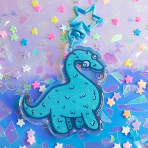 May include: A blue dinosaur keychain with a sparkly finish. The keychain is attached to a silver star charm.
