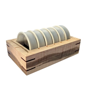 May include: A wooden box with six white plastic rings inside. The box is made of maple wood with a natural finish.