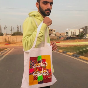 May include: A white tote bag with a colorful patchwork design and Arabic calligraphy that reads "Ramadan Kareem".