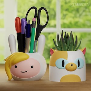 Pode incluir: Dois organizadores de mesa de cerâmica em forma de personagens de desenhos animados. O primeiro é um Finn o Humano branco e rosa de Hora de Aventura com cabelo amarelo e um rosto sorridente. O segundo é um Jake o Cão branco e amarelo de Hora de Aventura com olhos azuis e um rosto sorridente. O organizador Finn contém canetas e lápis, enquanto o organizador Jake contém uma pequena planta suculenta.