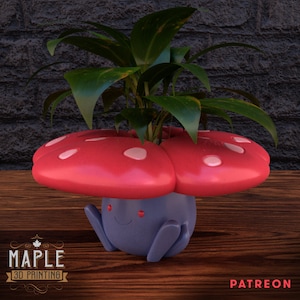 May include: A red and white mushroom-shaped planter with a blue and purple character face, holding a green plant.