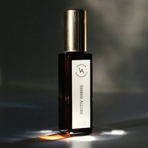 May include: A brown glass bottle of perfume with a gold cap. The label reads "V. Atelier" and "Serene Allure" with the text "eau de parfum 10 ml 0.33 fl oz".