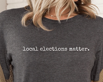 May include: Dark heather grey t-shirt with the text "local elections matter." printed in white.