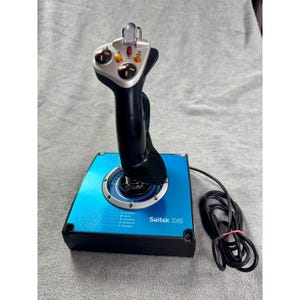 Könnte beinhalten: Ein schwarz-silberner Saitek X45 Flugsteuerungs-Joystick mit einer blauen Basis, weißen Textbeschriftungen, mehreren orangefarbenen Tasten, einem roten Feuerknopf und einem silbernen Abzug. Ein schwarzes Kabel ist an der Basis befestigt.