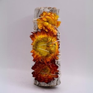 Könnte beinhalten: Weißer Salbei-Reinigungsstab, umwickelt mit drei getrockneten Blumen. Die Blumen sind orange, gelb und rot.