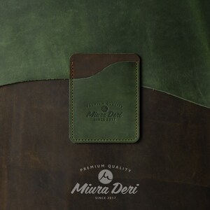 Puede incluir: Un porta tarjetas de cuero verde con una solapa de cuero marr&oacute;n y un logotipo cosido que dice "Premium Quality Miura Deri Since 2017".