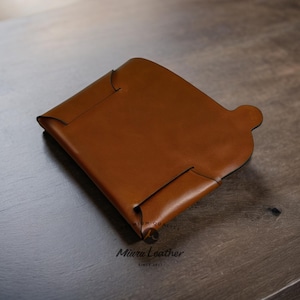 K&ouml;nnte beinhalten: Ein braunes Lederportemonnaie mit einem Klappdeckel und einer kleinen Tasche auf der Vorderseite. Die Brieftasche wird von Miura Leather hergestellt, seit 2017.