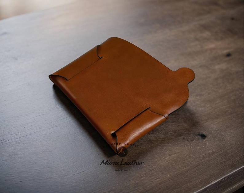 K&ouml;nnte beinhalten: Ein braunes Lederportemonnaie mit einem Klappdeckel und einer kleinen Tasche auf der Vorderseite. Die Brieftasche wird von Miura Leather hergestellt, seit 2017.