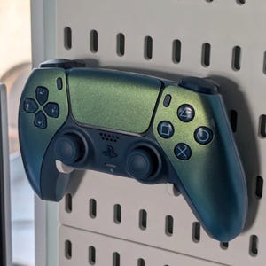 Può includere: Un controller di gioco personalizzato con una finitura sfumata, che passa dal verde acqua al verde. Il controller presenta il layout dei pulsanti standard ed è montato su una parete forata bianca.