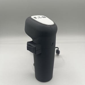 May include: A black and white gear shifter with a white button and the word "ETON" printed on the top. The shifter has a black cord attached to it.