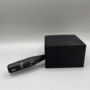 Puede incluir: Pieza de coche negra con una palanca y varios botones. La palanca tiene marcas para "Auto", "Apagado" y "Encendido". Los botones tienen símbolos para los faros, los faros antiniebla y una bocina.