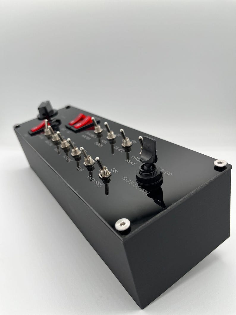 May include: A black rectangular flight simulator switch panel featuring multiple metal toggle switches, two red rocker switches, and a black landing gear lever. The panel surface is labeled with white text including LANDING, GEAR DOWN, and PITOT HEAT.