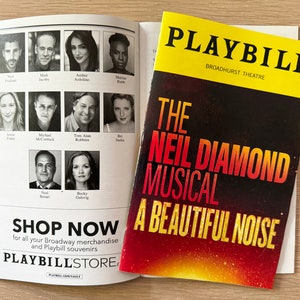 May include: Playbill for the Neil Diamond musical "A Beautiful Noise" at the Broadhurst Theatre. The cover features a red, yellow, and black design with the title of the show in large, bold letters. The Playbill also includes a cast list and a shop now button.