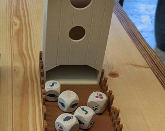 May include: A brown wooden birdhouse with a brown roof and two holes. The birdhouse is sitting on a brown wooden tray with a brown fence around the edge. There are six dice inside the tray, each with a different animal or food image on it.