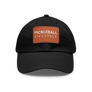 May include: A black baseball cap with a brown leather patch that says "Pickleball Lifestyle" in white text.