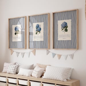 Puede incluir: Tres impresiones enmarcadas con ilustraciones botánicas de hortensias azules y texto bíblico. Los marcos tienen un acabado de madera clara y están colocados sobre un fondo a rayas azules y blancas. Una guirnalda de pequeñas banderas cuelga debajo.