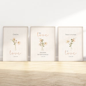 May include: Three printable wall art prints featuring floral illustrations and bible verses. The first print reads "God is love" with a floral illustration. The second print reads "We love because he first loved us" with a floral illustration. The third print reads "There is no fear in love" with a floral illustration.
