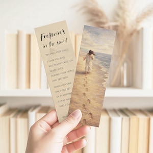 May include: Two bookmarks are held in a hand. One bookmark features the text "Footprints in the sand" and a poem. The other bookmark has an image of a person walking on a beach with footprints in the sand.