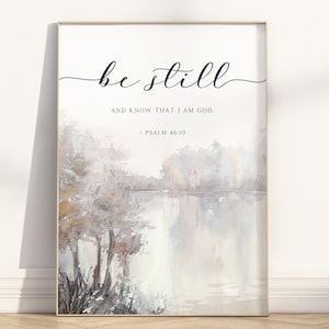 Può includere: Stampa artistica incorniciata con le parole "be still" in elegante scrittura sopra il testo "AND KNOW THAT I AM GOD. - PSALM 46:10." L'opera presenta un paesaggio ad acquerello di un lago e alberi in toni tenui.