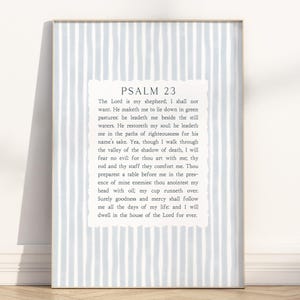 May include: Framed print featuring Psalm 23 text on a light blue and white striped background. The text is displayed in a white, decorative frame. The print is leaning against a white wall.