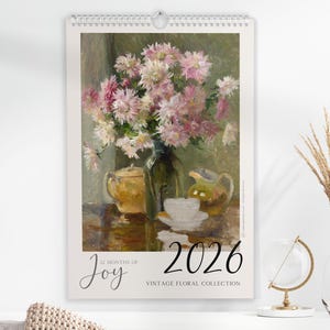 Könnte beinhalten: Wandkalender 2026 mit einem Vintage-Stillleben mit Blumen. Das Kunstwerk zeigt einen Strauß rosa und weißer Blumen in einer Vase, mit Teetassen und einer Teekanne. Der Kalender enthält den Text "12 Months of Joy" und "Vintage Floral Collection."