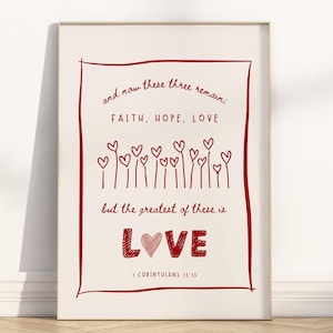 May include: A white framed print with a red border and red text that reads "and now these three remain: FAITH, HOPE, LOVE but the greatest of these is LOVE 1 CORINTHIANS 13:13". The text is surrounded by a row of red hearts.