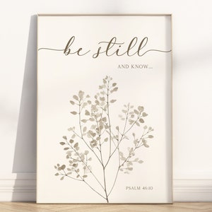 Op de afbeelding: Een ingelijste print met de woorden "be still" in elegant schrift boven de zin "and know..." en een botanische illustratie. De onderkant van de print luidt "Psalm 46:10". Het kunstwerk heeft een neutraal kleurenpalet.