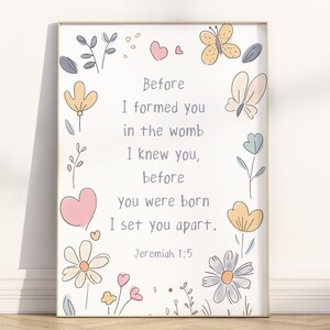 Puede incluir: Impresión enmarcada con un fondo claro, con el texto «Antes de formarte en el vientre, te conocí, antes de que nacieras, te consagré. Jeremías 1:5». Decorada con flores, mariposas y corazones en colores pastel.