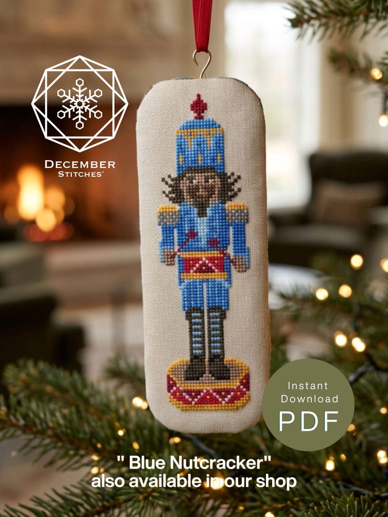 May include: A rectangular cross-stitch ornament featuring a nutcracker in a blue uniform with a red drum, yellow accents, and black boots. The design is on light fabric with a red ribbon hanger. Text includes DECEMBER STITCHES and Instant Download PDF.