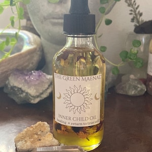 May include: A glass bottle with a dropper filled with a yellow liquid and dried flowers. The label reads "The Green Maenad Inner Child Oil healing * return to true self".