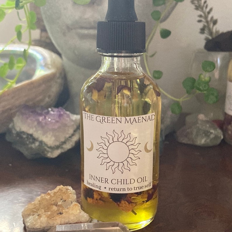 May include: A glass bottle with a dropper filled with a yellow liquid and dried flowers. The label reads "The Green Maenad Inner Child Oil healing * return to true self".