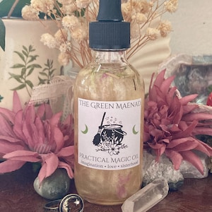 May include: A glass bottle of Practical Magic Oil by The Green Maenad. The bottle is filled with a clear liquid and has a dropper top. The label is white with green text and a black and white illustration of a cauldron and a broom.