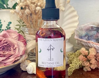 May include: A glass bottle of oil with a black dropper top and a white label that reads "The Green Maenad Beltane Oil Passion * Fertility * Creativity". The bottle is filled with a red liquid and contains dried flowers.
