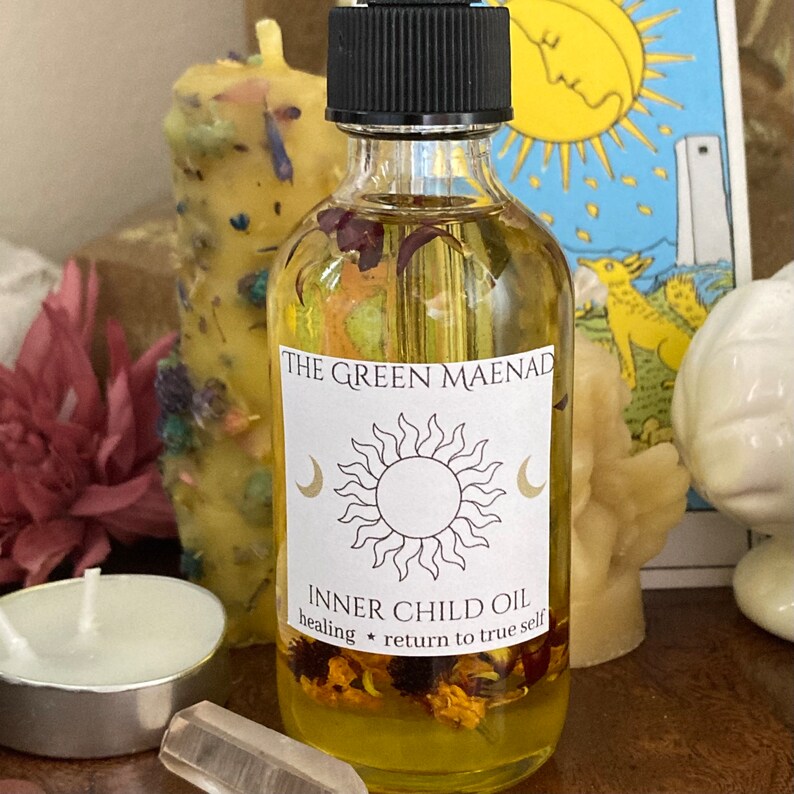 May include: A glass bottle of Inner Child Oil by The Green Maenad. The label is yellow with a sun and moon design. The text on the label reads "Inner Child Oil healing * return to true self".