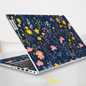 May include: A navy blue laptop with a floral pattern on the lid. The pattern features pink, yellow, and white flowers on a dark blue background. The laptop has the Lenovo logo on the lid.