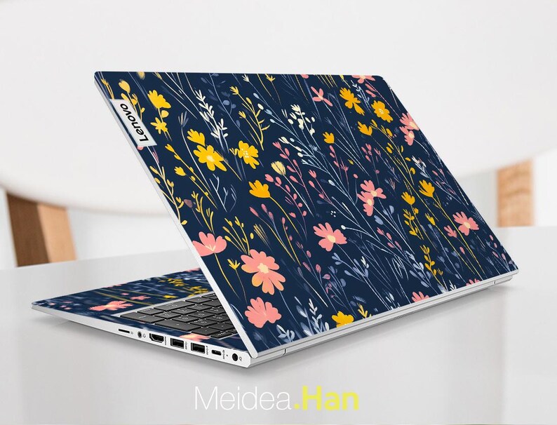 May include: A navy blue laptop with a floral pattern on the lid. The pattern features pink, yellow, and white flowers on a dark blue background. The laptop has the Lenovo logo on the lid.