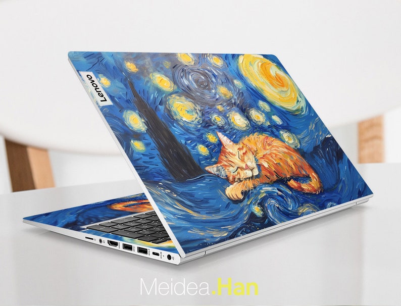 May include: A white laptop with a blue and yellow starry night design featuring a sleeping orange cat. The laptop has the Lenovo logo on the back.