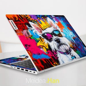 May include: A white laptop with a colourful, abstract design featuring a dog wearing sunglasses and a crown. The design includes splashes of pink, blue, yellow, and green paint. The laptop has the word "Lenovo" on the back.