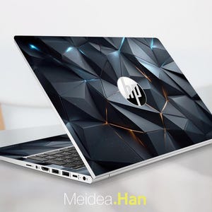May include: A silver HP laptop with a geometric design on the lid. The design features a dark gray, faceted pattern with accents of gold and blue. The HP logo is centered on the lid. The text "Meidea.Han" is at the bottom.