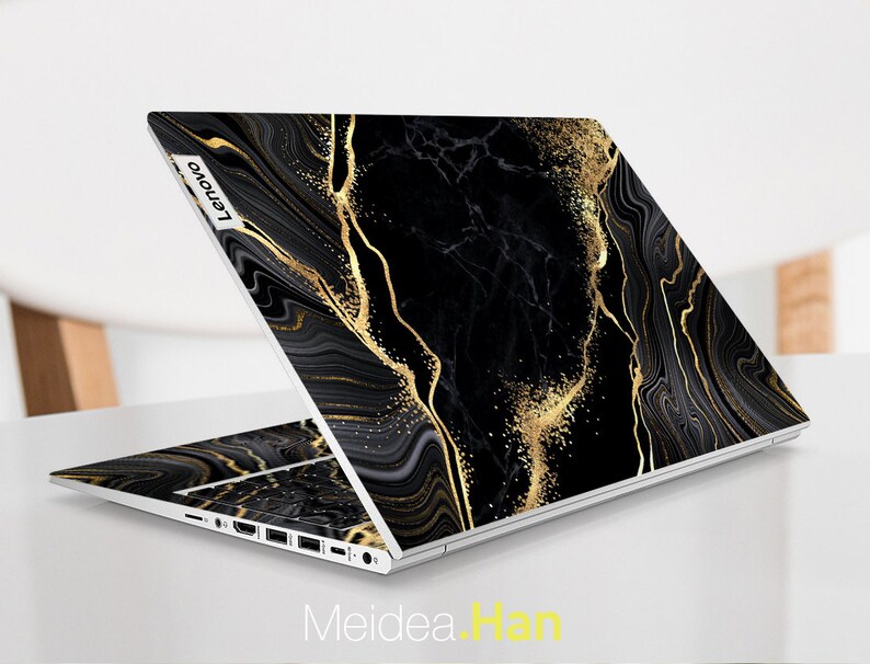 Puede incluir: Port&aacute;til negro con un dise&ntilde;o de m&aacute;rmol dorado y negro. El port&aacute;til tiene el logotipo de Lenovo en la parte posterior.