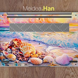 Op de afbeelding: Een laptop skin met een kleurrijk schelpdesign. De skin toont een zonsondergang boven de oceaan met golven die op de kust breken. De schelpen zijn in tinten roze, wit en bruin.