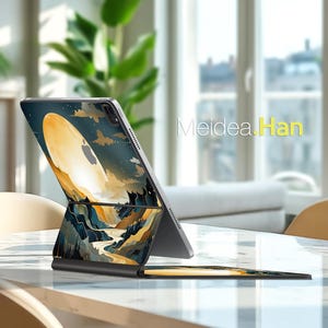 Puede incluir: Una funda para iPad con un diseño de paisaje que presenta una gran forma ovalada brillante sobre un fondo de montañas y un río. La funda es negra y tiene el texto "Meidea.Han".