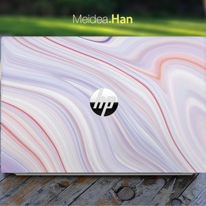 Könnte beinhalten: Ein weißer Laptop mit einem wirbelnden rosa und weißen Marmormuster auf dem Deckel. Das HP-Logo befindet sich in der Mitte des Deckels.